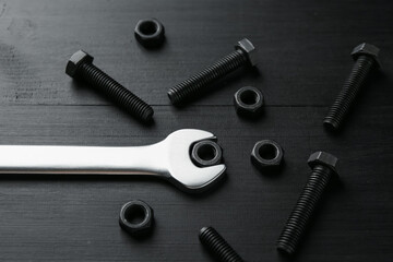 Metal wrench, bolts and nuts on black wooden table, above view