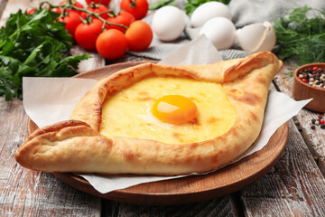 Tasty khachapuri with cheese, egg and other products on wooden table, closeup