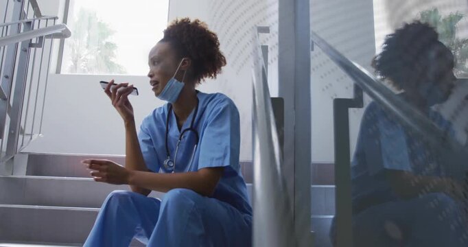 Nurse settling on medical stair landing pulling mask down and starting speakerphone call on break