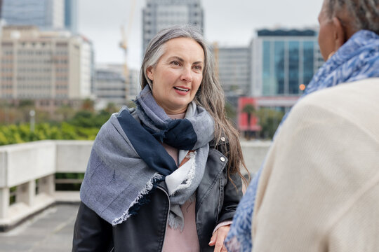 Senior and mature women friends chatting on terrace by concrete railing in leather jacket