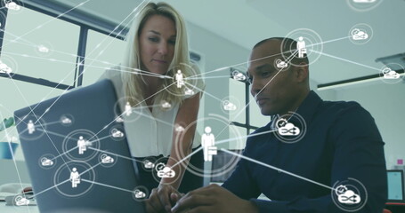 Collaborating coworkers in office attire leaning over laptop typing at desk, network icon overlay