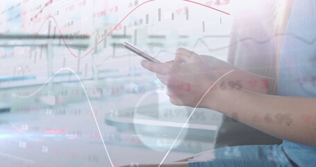 Woman in blue dress checking stock charts on smartphone at office desk, with monitor, copy space