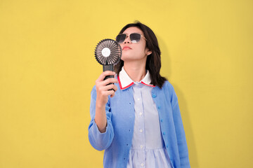 Obraz premium A confident young woman cooling herself with a hand-held fan while wearing sunglasses