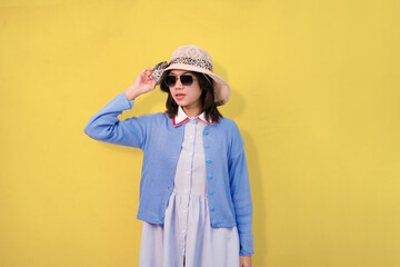 Confident woman casually wearing a fashionable blue cardigan, sunglasses, and a straw hat showing summer concept and travel