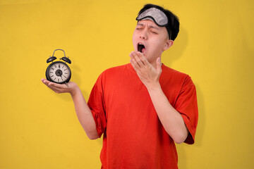 man waking up tired holding alarm clock against yellow background
