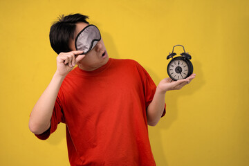 man waking up tired holding alarm clock against yellow background