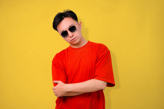 confident young man wearing sunglasses standing against yellow and orange background