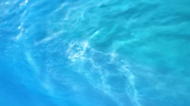 A bright blue water surface with subtle ripples and shimmering light reflections creating movement