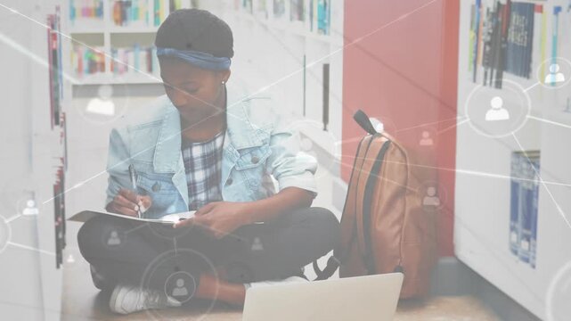 Student writing notes with laptop in library while network icons emerging showing digital learning