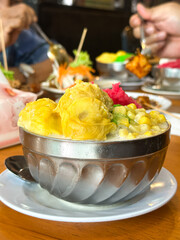 Cendol, a Malaysian ice dessert with durian, sticky rice, corn, and jelly in creamy coconut base, served in metal bowl on white saucer.