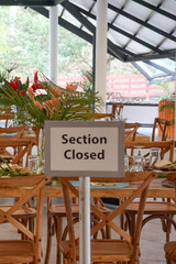 Dining area with wooden tables, glassware, and flowers, marked “Section Closed” in a semi-outdoor setting with lush greenery.