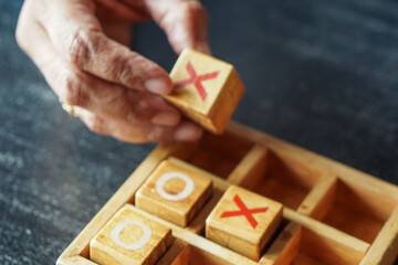 Close-up of hand holding wooden block with red X above tic-tac-toe grid, highlighting tactile play and handcrafted design.