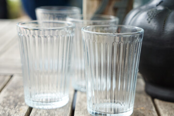 Four clear, vertically ribbed drinking glasses arranged on a weathered wooden table with a blurred background, highlighting texture and transparency.
