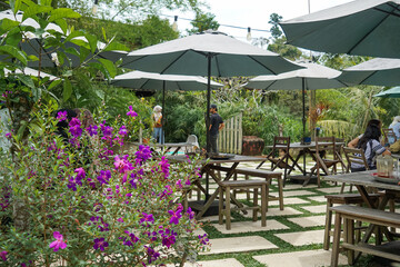 Obraz premium Rustic outdoor café seating with wooden table, benches, potted plants, and lush greenery in a cozy garden setting.