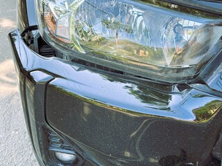 Obraz premium A close-up view shows the black car's damaged and dented bumper on the front due to a traffic accident.