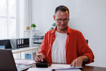 Obraz premium Business man Using laptop computer and working at office with calculator document on desk, doing planning analyzing the financial report, business plan investment, finance analysis concept. 
