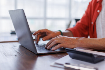 Business man Using laptop computer and working at office with calculator document on desk, doing planning analyzing the financial report, business plan investment, finance analysis concept.
