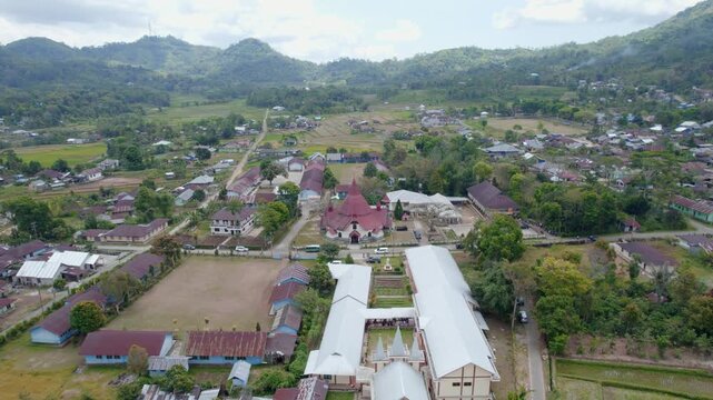 Drone aerial footage of a red roof church in Ruteng, Flores, Indonesia. The video shows the church surrounded by village houses, rice fields, and green mountains in the background.
