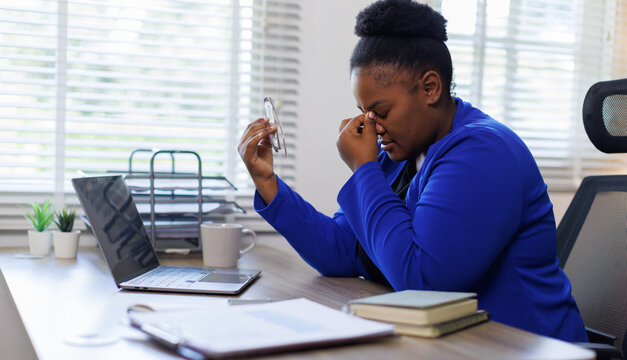 Woman, desk and stress in office with headache, fatigue and overworked migraine pain and technology for frustrated employee in workplace.

