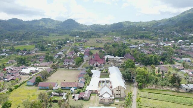 Drone aerial footage of a red roof church in Ruteng, Flores, Indonesia. The video shows the church surrounded by village houses, rice fields, and green mountains in the background.
