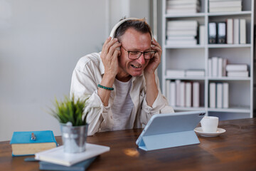 Happy american man in wireless headphones working on computer, watching webinar, looking at screen and smiling. Cheerful  male freelancing, taking part in online conference
