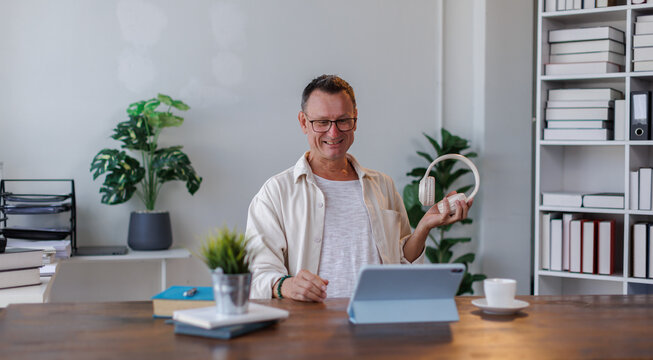 Happy american man in wireless headphones working on computer, watching webinar, looking at screen and smiling. Cheerful male freelancing, taking part in online conference