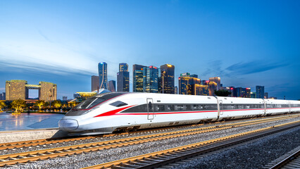 Modern high-speed train running through an urban area with skyscrapers in the background © zhouyilu