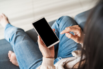 Young woman using smart phone and relaxing on sofa in living room at cozy home in the morning