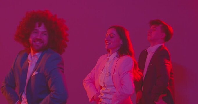 Funny people dance and cheerfully imitate movements of chicken, filling dance with humor and fun. Men and women in colorful suits wave their hands funny while dancing on dance floor in neon light. 