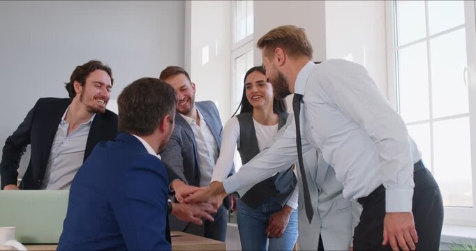 Group of a positive business people celebrating success together in an office. The team forms a circle, sharing high fives and holding hands, teamwork through unity and achievement.