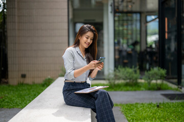 Fototapeta premium Smiling businesswoman using smartphone while sitting outdoors with documents