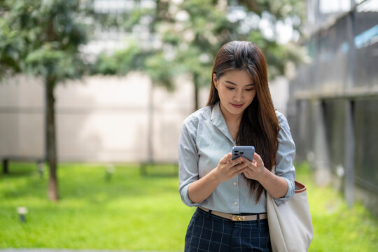Businesswoman using smartphone in urban park: enjoying mobile technology outdoors - Powered by Adobe
