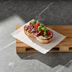 Roast beef bruschetta with tomatoes on bright rustic overhead composition, marble and wood surfaces