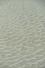 Close-up of rippled sand dunes, showing texture and natural patterns. Uneven sand texture, beach background, top down view. Closeup shot of sand texture on the beach as background.