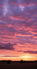 A vibrant sunset sky filled with hues of pink and purple, with a field in the foreground.