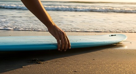 Close-up of a hand picking up a surfboard resting on wet sand at the beach, surfing concept, outdoor sports, summer vibe