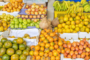 Colorful fresh fruit stand at a local market featuring oranges, tamarillos, coconuts, bananas, red and green apples, dragon fruit, and granadillas. Perfect for themes of tropical nutrition, Ecuadorian