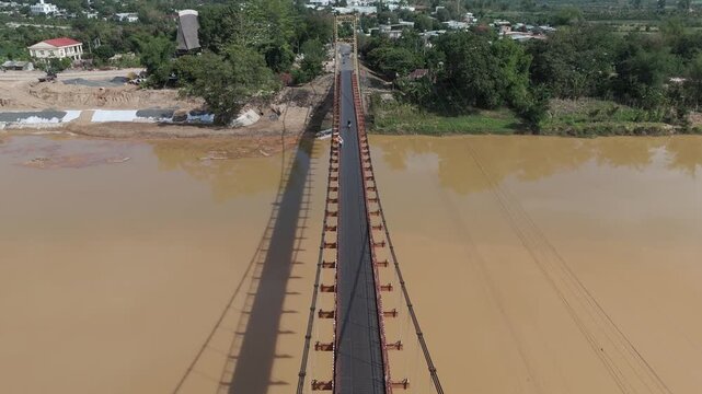 Drone footage above an old suspension bridge in Kon Tum, central highlands, Vietnam. Camera is moving foward above the traffic on the structure.