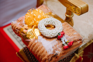 Close-up of a stack of orange monk's robes, neatly folded on an ornate silver pedestal, with other elements in the background.