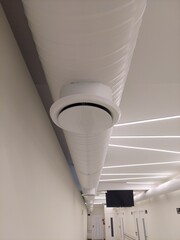 A low-angle, detailed view of a ceiling-mounted ventilation system, featuring a large, white, spiral-ribbed air duct and a circular vent. The image focuses on the modern HVAC engineering and design, w