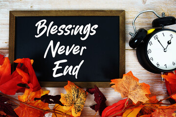 Blessings Never End text written on chalkboard with alarm clock and maple leaf decoration on wooden...