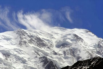 Obraz premium Snow-capped mountain peak under a vibrant blue sky with windswept clouds