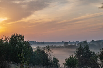Hilly plain covered in fog, illuminated by the dawn sun.