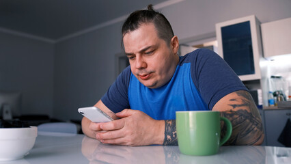 A brutal guy is sitting at the kitchen table, drinking coffee and chatting on his phone. A male freelancer solves important cases