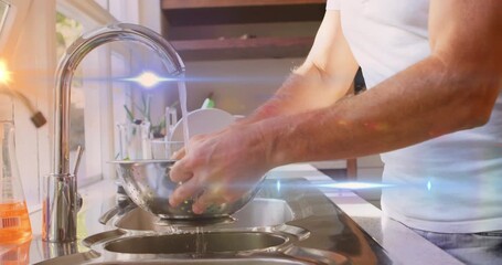 Animation of light spots and trails over caucasian man washing vegetables in kitchen - Powered by Adobe