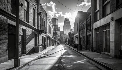 Black and white shot of a city street fading into tall buildings under a sunlit sky, casting long shadows on the road