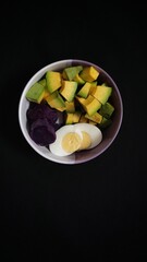 Bowl of Healthy Food with Avocado, Egg and Purple Potatoes on Black Background