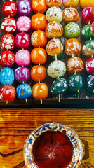 Fototapeta premium Rows of vibrant, colorful candies on sticks, displayed neatly. A bowl with dipping sauce enhances this sweet street food.
