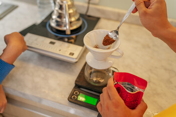 Hands carefully measuring coffee grounds for brewing purposes on a digital scale device