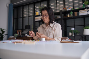 Mature asian woman making handmade jewellery accessories handcraft hobby